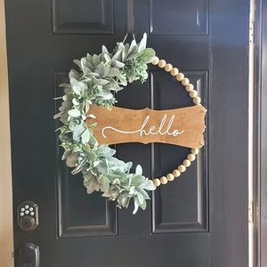 Detail of wooden bead wreath with faux greenery and hello sign on a black door