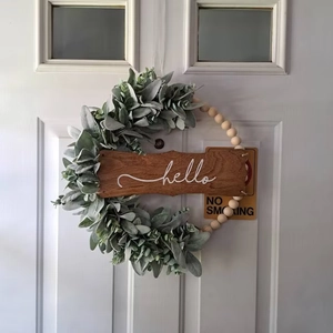 Detail of eucalyptus wreath with wooden beads and white script hello on a dark wood sign