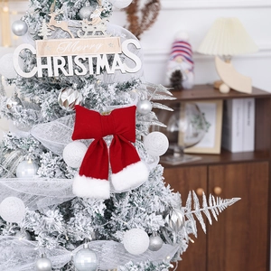 Close-up of a large red velvet Christmas bow with white faux fur trim on a snowy tree