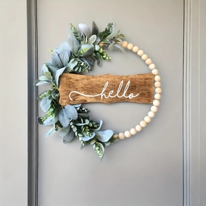Close-up of wood bead wreath with green leaves and a hello sign on a grey door