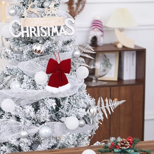 Close-up of a large red velvet Christmas bow with white fur trim hanging on a snowy tree