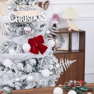 Detail of a large red velvet Christmas bow hanging on a white frosted tree with ornaments