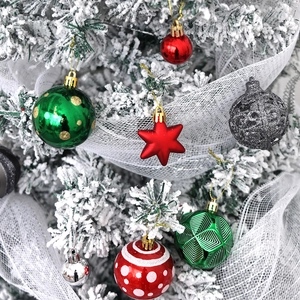 Details von sortierten Weihnachtskugeln und einem roten Stern auf verschneitem Baum