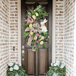 Easter floral wreath with bunnies and jute bow hanging on a dark wooden door for decor