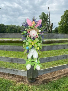 Osterhasenkranz mit Lavendel, bunten Eiern und gestreiften Schleifen am Holzzaun
