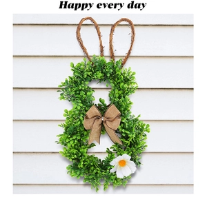Detail of Easter bunny wreath with green leaves and a brown burlap bow on white wood