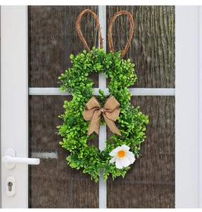 Close-up of Easter bunny-shaped wreath with green leaves and burlap bow on door