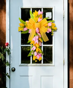 Dettaglio ghirlanda a croce con tulipani rosa e gialli e grande fiocco in tela di iuta