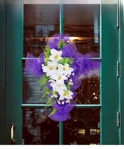 Dettaglio della ghirlanda a croce in rete viola con gigli bianchi su porta in legno