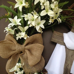 Easter wreath with wooden cross, white lilies and burlap bow on grapevine base