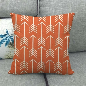 Orange linen square throw pillow cover with white arrow pattern on a grey sofa