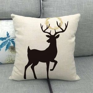Linen Christmas reindeer pillow cover with elk silhouette and floral wreath on a sofa