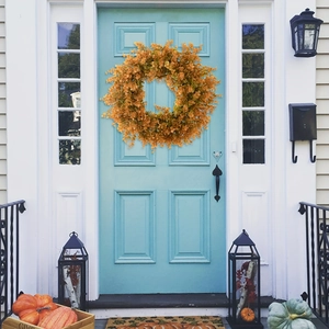 Autumn orange eucalyptus wreath hanging on a blue front door with harvest pumpkins