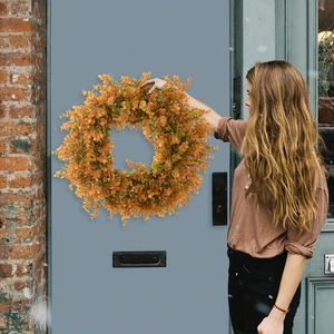 Autumn eucalyptus wreath with warm orange leaves held against a blue vintage door
