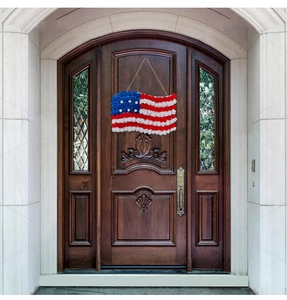 Patriotic USA flag rose wreath hanging on a brown wooden front door for holiday decor