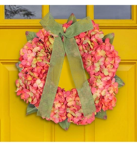 Detail of pink and green hydrangea wreath with a mesh bow hanging on a yellow door