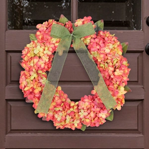 Artificial hydrangea wreath with pink petals and green burlap bow on a brown wooden door