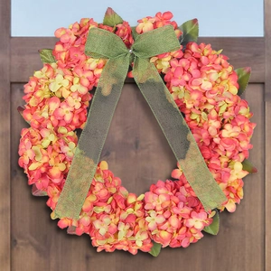 Autumn hydrangea wreath with orange petals and green burlap bow on dark wooden door