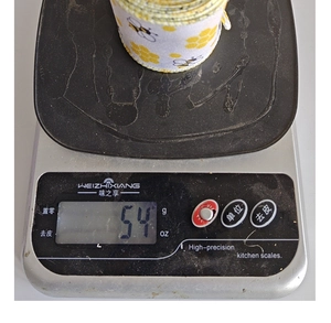Nahaufnahme einer 54g Rolle Sackleinenband mit Bienenmuster auf einer Waage
