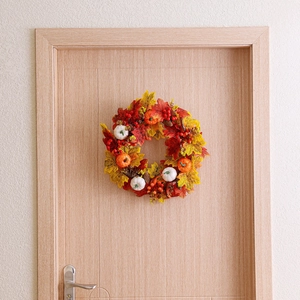 Close-up of autumn wreath featuring white pumpkins, maple leaves, and pine cones