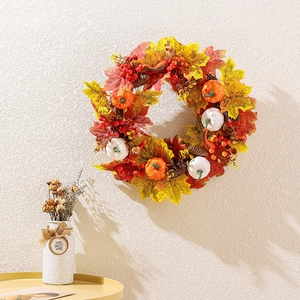Autumn wreath with white pumpkins, maple leaves, and berries on a white textured wall
