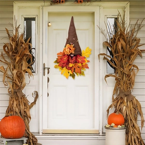 Detail of autumn gnome door wreath with faux maple leaves and rustic flowers on a white door