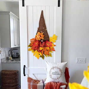 Detail of fall gnome wreath with colorful maple leaves hanging on a white wooden barn door