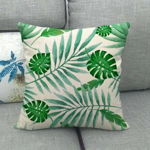 Detalle de funda de cojín de lino con estampados de hojas tropicales sobre un sofá gris