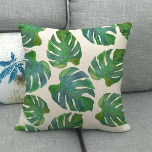 Detalle de estampado de hoja de monstera en funda de cojín de lino sobre un sofá gris