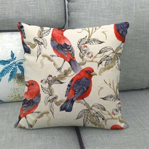 Linen cushion cover with watercolor red birds and floral pattern on a gray sofa
