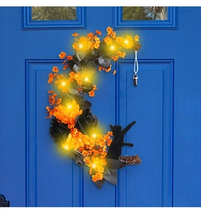 Detail of moon wreath with black cat silhouette, orange flowers and LED light on a door
