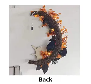 Detail of moon-shaped Halloween wreath featuring orange flowers and black cat pendant