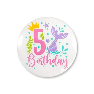 Detailed close-up of mermaid theme 5th birthday badge with glitter tail and crown