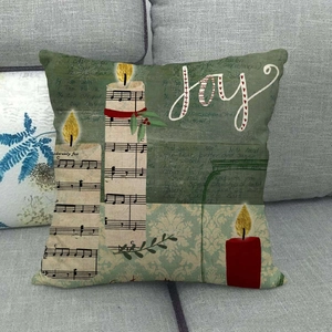 Détail d'une housse de coussin de Noël en lin avec lettrage Joy, bougies et partition