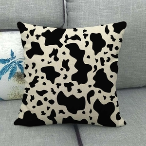 Close-up of square linen throw pillow case featuring classic black and white cow spots
