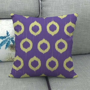 Close-up of geometric purple and yellow tie-dye ikat pillow cover on a grey sofa