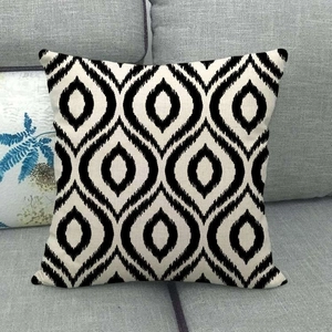 Square linen cushion cover with black and white geometric diamond ikat pattern on a sofa