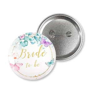Close-up of floral Bride to Be tinplate badge with gold script and watercolor butterfly