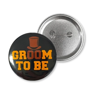 Macro view of Groom To Be tinplate badges showing front design and pin-back structure