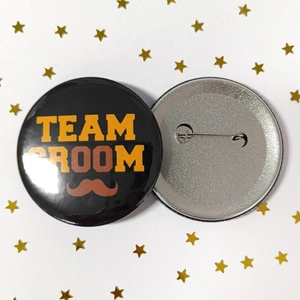 Detailed view of Team Groom tinplate badges with secure safety pin backing