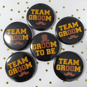 Close-up of Team Groom and Groom to Be tinplate badges with retro typography