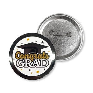 Front and back detail of tinplate graduation badges with Congrats GRAD and safety pin