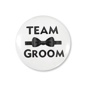Dettaglio della spilla tonda Team Groom in latta con papillon nero per matrimoni