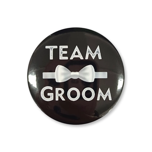 Dettaglio spilla nera Team Groom con logo papillon bianco per addio al celibato maschile