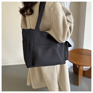 Detail of a large black canvas tote bag showing side pocket and front zipper on model