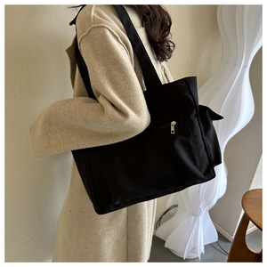 Detail of black canvas tote bag with side zipper pocket shown on a beige wool coat