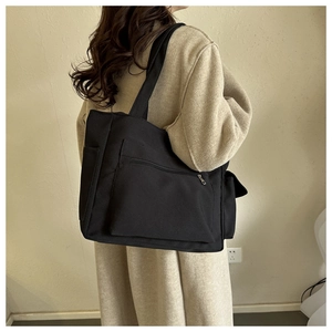 Detail view of black canvas tote bag with multiple pockets and wide shoulder strap