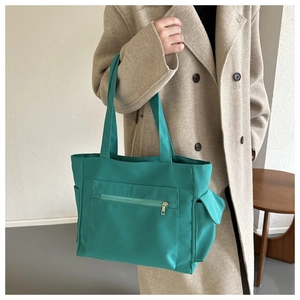 Detail of emerald green canvas tote bag showing wide straps and front zipper pocket detail