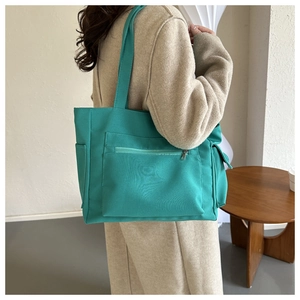 Detail of teal canvas tote bag with front zipper and side pocket on a model