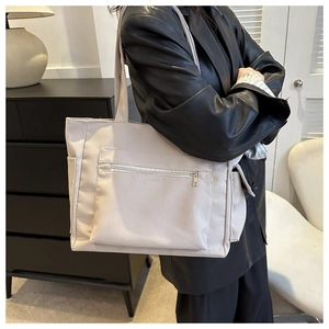 Detailed shoulder view of a beige oversized tote bag with functional zipper and side pockets